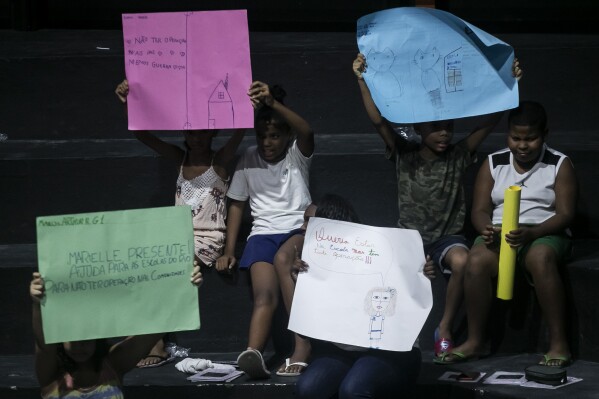 Unos niños sostienen dibujos que representan sus experiencias de vida en la favela Maré durante la presentación del libro titulado "Se suponía que tenía que estar en la escuela" en la favela Maré de Río de Janeiro, Brasil, el lunes 25 de marzo de 2024. (AP Foto/Bruna Prado)