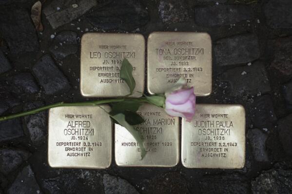 A flower lays on polished so-called 'Stolpersteine' or 'stumbling stones' commemorating people deported and killed by the Nazis in front of a resident building in Berlin, Germany, Tuesday, Nov. 9, 2021, the 83th anniversary of the Nazis' anti-Jewish pogrom in 1938. The stones are among thousands set into sidewalks in front of houses in Germany and other European countries where victims of the Nazis lived or worked before they were deported and killed. The inscriptions include the names of the victims, the dates of their birth and of their deportation and murder. To stones are cleaned by residents on and around the Nov. 9 anniversary. (AP Photo/Markus Schreiber)
