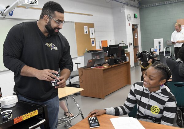 FILE - Baltimore Ravens lineman and math scholar John Urschel, left, hands out ice cream to Chelsy Valerio, 14, of Baltimore, during a lesson at Dundalk High School during the launch of Texas Instruments' STEM Behind Cool Careers series in Baltimore, in this Tuesday, July 18, 2017, file photo. John Urschel has found that a master's degree in mathematics, his stature as an accomplished author and his pending PhD at MIT isn't necessarily enough to sell young students on the benefit of crunching numbers. What really makes him interesting to most kids is that he's a former NFL player who opted to immerse himself in math. (Steve Ruark/AP Images for Texas Instruments, File)
