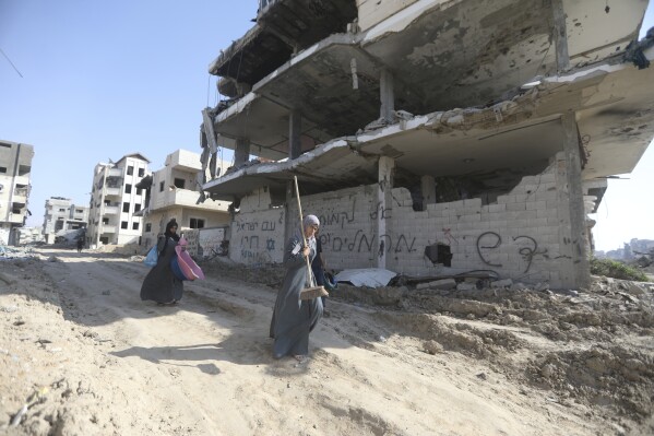 فلسطينيون يسيرون وسط الدمار الذي خلفه الهجوم الجوي والبري الإسرائيلي بعد انسحابهم من خان يونس، قطاع غزة، الأحد، 7 أبريل، 2024. كتابات عبرية على الحائط تقول "شعب إسرائيل يعيش" (صورة AP/إسماعيل أبو دية)