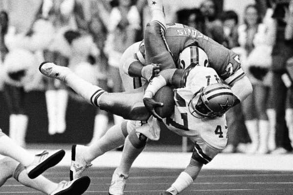 
              FILE - In this Jan. 9, 1983, file photo, Dallas Cowboys safety Dextor Clinkscale (47) is upended by Tampa Bay Buccaneers offensive tackle Dave Reavis after his interception and 11-yard return during the first quarter of an NFL football playoff game in Irving, Texas. Clinkscale is one of 60 singers--all former NFL players and a couple of current ones--who will participate in the 20th Super Bowl Gospel Celebration at Atlanta Symphony Hall on Thursday night. The choir is set to perform two songs at the sold-out event that’s being televised Saturday. (AP Photo/Bill Haber, File)
            
