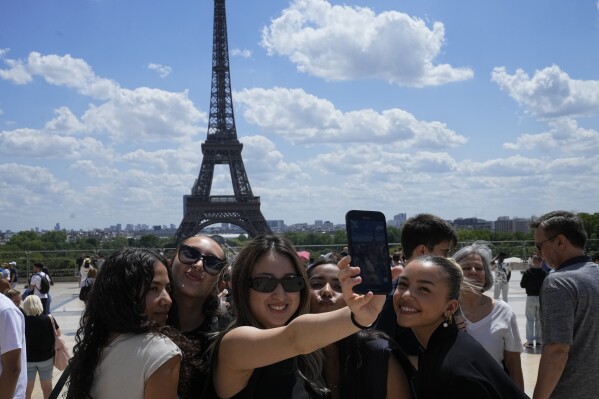 Tourists pose for a selfie with the Eiffel Tower in background, Thursday, July 6, 2023 in Paris. French government officials met with representatives of the tourism industry to discuss repercussions of unrest sparked by the police killing of a 17-year-old boy on tourist activity and on France's international image. The shooting death of Nahel Merzouk, who was of north African descent, prompted nationwide anger over police tactics and entrenched discrimination against people in low-income neighborhoods around France where many trace their roots to former French colonies. (AP Photo/Michel Euler)