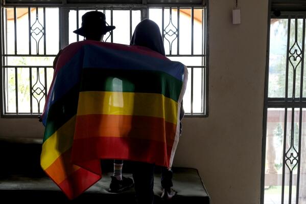FILE - A gay Ugandan couple cover themselves with a pride flag as they pose for a photograph in Uganda on March 25, 2023. Ugandan lawmakers on Tuesday, May 2, 2023 passed a new version of an anti-gay bill that removes a clause which appeared to criminalize identifying as LGBTQ. (AP Photo, File)