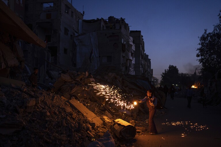 A Palestinian boy plays with fireworks as he celebrates the start of the Muslim holy month of Ramadan next to a destroyed residential building by the Israeli airstrikes in Rafah, Gaza Strip, Sunday, March 10, 2024. (AP Photo/Fatima Shbair)