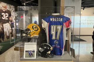 This photo shows a display with Jen Welter's blue-and-pink jersey, Friday, Aug. 5, 2022 in Canton, Ohio. A 15-year-old boy made his way through the The Pro Football Hall of Fame museum on Friday, checking out the memorabilia and bronze busts before stopping to take a picture of Jen Welter’s blue-and-pink jersey to send to his younger sister. (AP Photo/Rob Maaddi)