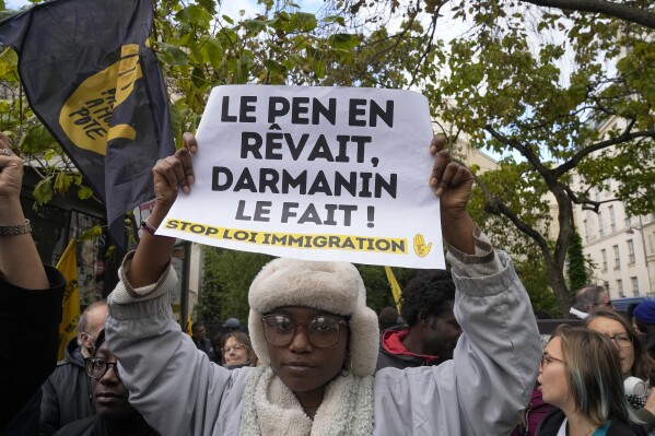 A protestor holds a paper reading : « Le Pen dreamed of it, Darmanin does it » during a demonstration in front of the Senate in Paris, Monday, Nov. 6, 2023. French senators start debating on Monday a divisive bill meant to toughen the country's immigration law that has been criticized as a threat to the rights of asylum seekers and other migrants. (AP Photo/Michel Euler)