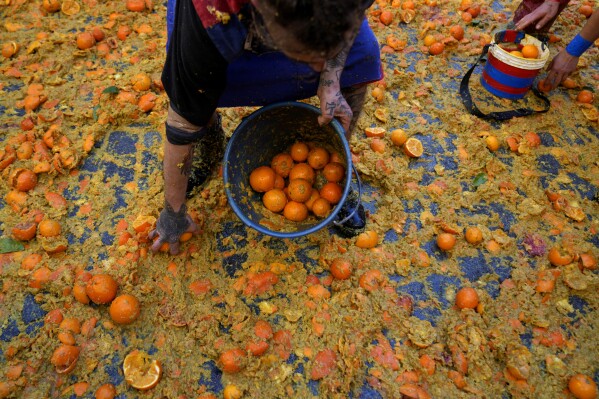 A man holds a bucket of oranges during the "Battle of the Oranges" where people pelt each other with oranges as part of Carnival celebrations in the northern Italian Piedmont town of Ivrea, Italy, Tuesday, Feb. 13, 2024. (AP Photo/Antonio Calanni)