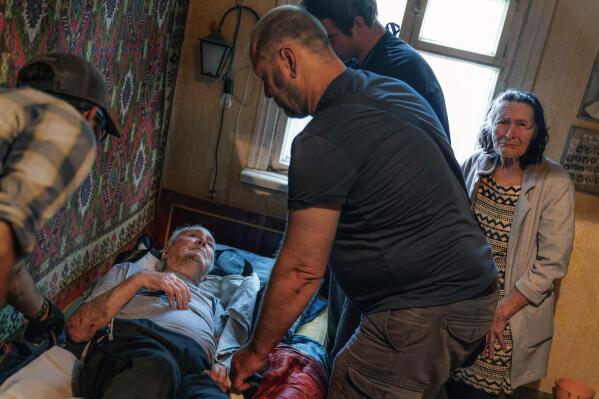 Lidia Mariukha, 79, right, weeps while her husband, Viktor, 84, is lifted out of his bed by members of the aid organization Refugease as they are evacuated from their home in Kramatorsk, Donetsk region, eastern Ukraine, Tuesday, Aug. 2, 2022. (AP Photo/David Goldman)