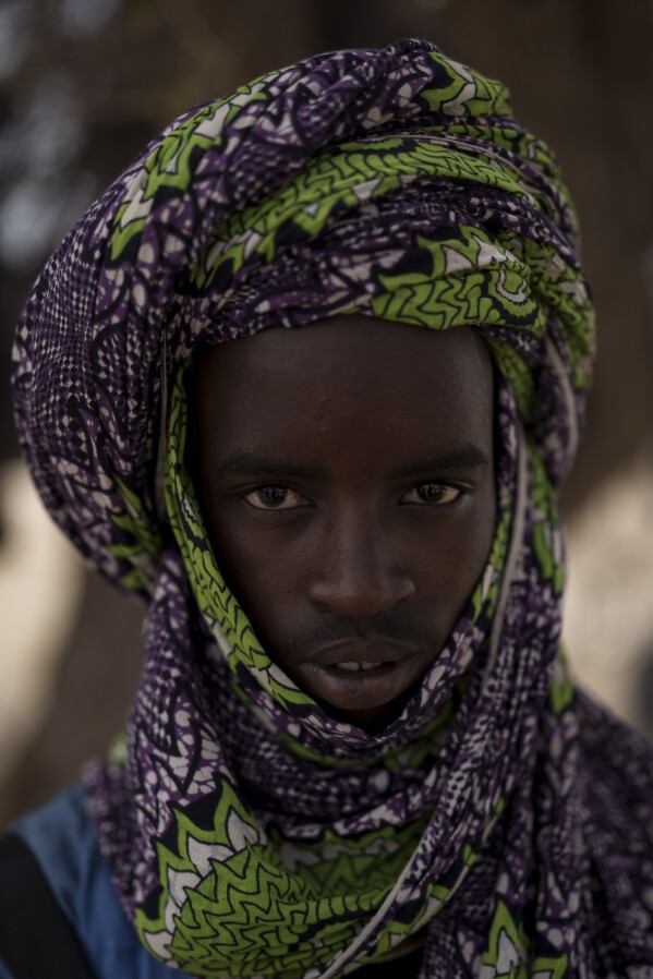 Abba Diallo, 18, stands for a portrait at a local market near a water station known as Bem Bem, in the Matam region of Senegal, Wednesday, April. 19, 2023. Diallo says that the vaccines to treat or prevent animals from disease are expensive, and during the lean season you have to fatten the cattle. "To raise livestock is hard. You follow the herd from morning to night without eating anything, you just drink water", he says. (AP Photo/Leo Correa)