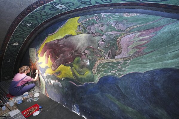 Art conservator Jessica Keister works on a mural by Maxo Vanka depicting the hand of God handing a tablet to Moses, inside St. Nicholas Croatian Catholic Church in Millvale, Pa., Wednesday, Feb. 19, 2025. (AP Photo/Gene J. Puskar)