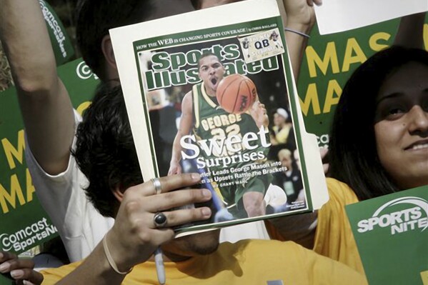 FILE - A George Mason University fan holds up a Sports Illustrated magazine at a send off for the team, March 29, 2006, in Fairfax, Va. Sports Illustrated is the latest media company damaged by being less than forthcoming about who or what is writing its stories. The website Futurism reported that the once-grand magazine used articles with 鈥渁uthors鈥� who apparently don't exist, with photos generated by AI. The magazine denied claims that some articles themselves were AI-assisted, but has cut ties with a vendor it hired to produce the articles. (AP Photo/Lawrence Jackson, File)
