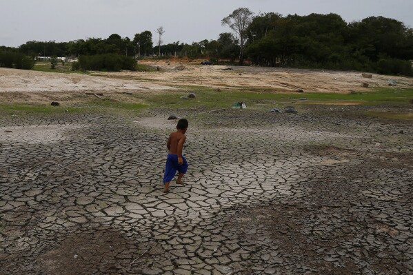 A little boy walks across a dry, cracked area of the Negro River near his houseboat during a drought in Manaus, Amazonas state, Brazil, Monday, Oct. 16, 2023. The Amazon’s second largest tributary on Monday reached its lowest level since official measurements began near Manaus more than 120 years ago. (AP Photo/Edmar Barros)