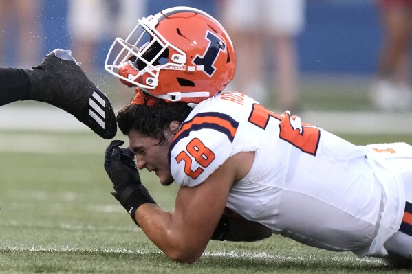 Illinois linebacker Dylan Rosiek loses his helmet while trying to tackle Kansas running back Devin Neal during the first half of an NCAA college football game Friday, Sept. 8, 2023, in Lawrence, Kan. (AP Photo/Charlie Riedel)