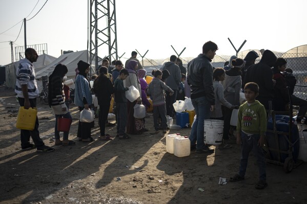 Members of the Abu Jarad family, who were displaced by the Israeli bombardment of the Gaza Strip, queue for water at a makeshift tent camp in the Muwasi area, southern Gaza, Monday, Jan. 1, 2024. (AP Photo/Fatima Shbair)