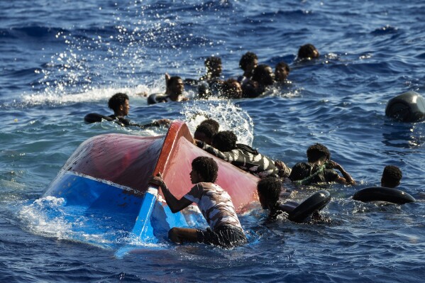 FILE - Migrants swim next to their overturned wooden boat during a rescue operation by Spanish NGO Open Arms at south of the Italian Lampedusa island at the Mediterranean sea, Aug. 11, 2022. Italy has impounded the Spanish charity rescue boat Open Arms in a Tuscan port for violating rules by Italy’s far-right-led government banning multiple rescues at sea, the charity said Thursday. Open Arms protested the sanctions as a violation of the law of the sea that requires boats to offer rescue, said it was being punished rescuing 176 people in three operations, including people of “extreme vulnerability.” (AP Photo/Francisco Seco, File)