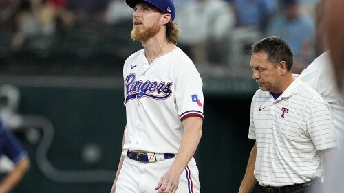Texas Rangers starting pitcher Jon Gray looks up as head athletic trainer Matt Lucero, right, checks on him after Gray was hit by a single off the bat of Tampa Bay Rays' Yandy Diaz in the fifth inning of a baseball game, Wednesday, July 19, 2023, in Arlington, Texas. Gray left the game with an unknown leg injury. (AP Photo/Tony Gutierrez)