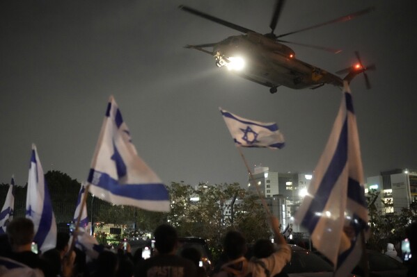 People wave Israeli flags as a helicopter carrying hostages released from Gaza by Hamas arrives at the helipad of the Schneider Children's Medical Center in Petah Tikva, Israel, Sunday, Nov. 26, 2023. (AP Photo/Leo Correa)