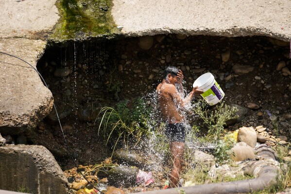 A man cools himself by taking a bath with water collected from a leaking municipal pipe on a hot summer day on the outskirts of Jammu, India, Friday, May 31, 2024. Officials say a scorching heat wave has killed at least 14 people, including 10 election officials, in eastern India with temperatures soaring up to 49.9 degrees Celsius (122 degrees Fahrenheit) in parts of India this week. (AP Photo/Channi Anand)