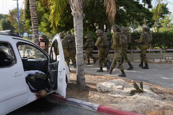 Israeli soldiers walk by a civilian killed by Hamas militants in Sderot, Israel, on Saturday, Oct. 7, 2023. Hamas militants in the Gaza Strip infiltrated Saturday into southern Israel and fired thousands of rockets into the country while Israel began striking targets in Gaza in response. (AP Photo/Ohad Zwigenberg)