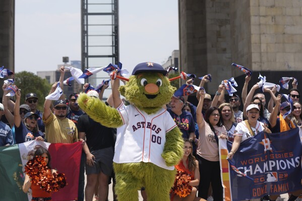 Houston Astros team mascot Orbit and fans, pose for a photo backdropped by the Monument to the Revolution in Mexico City, Thursday, April 25, 2024. The Houston Astros will face Colorado Rockies in two regular season game beginning Saturday, at Mexico City's Alfredo Harp Helú stadium. (AP Photo/Fernando Llano)