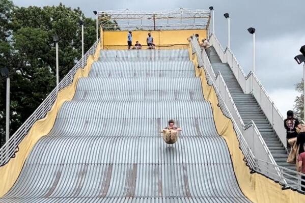 Attendees go down the giant slide at Belle Isle state park in Detroit on Friday, Aug. 26, 2022.  The slide re-opened after a slick surface sent people flying a week ago. Authorities scrubbed down the surface and sprayed water on the slide to help control the speed.  (Ed Pevos/MLive.com via AP)