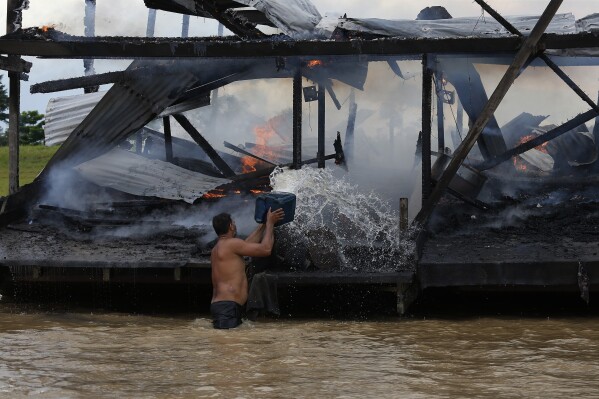 FILE - An illegal miner throws water at one of the more than 60 dredging barges that were set on fire by officers of the Brazilian Institute of the Environment and Renewable Natural Resources, IBAMA, during an operation to try to contain illegal gold mining on the Madeira river, a tributary of the Amazon river in Borba, Amazonas state, Brazil, Nov. 28, 2021. The two-day Amazon Summit opens Tuesday, Aug. 8, 2023, in Belem, where Brazil hosts policymakers and others to discuss how to tackle the immense challenges of protecting the Amazon and stemming the worst of climate change. (AP Photo/Edmar Barros, File)