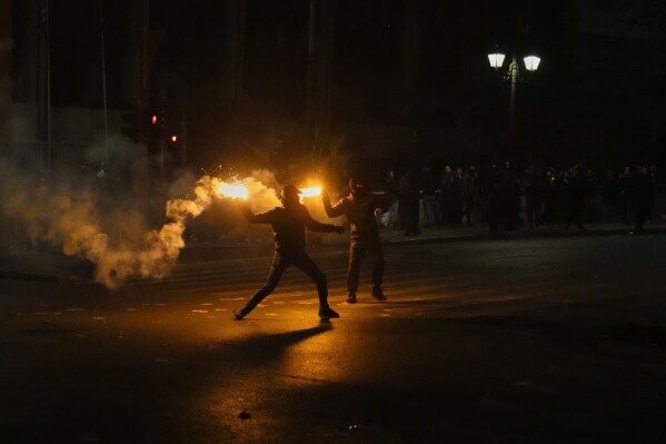 Hooded protesters throw flares against riot police during clashes, on the third and final day of a censure motion debate against the conservative government in parliament over a deadly rail disaster nearly two years ago, in Athens, Greece, Friday, March 7, 2025. (AP Photo/Petros Giannakouris)