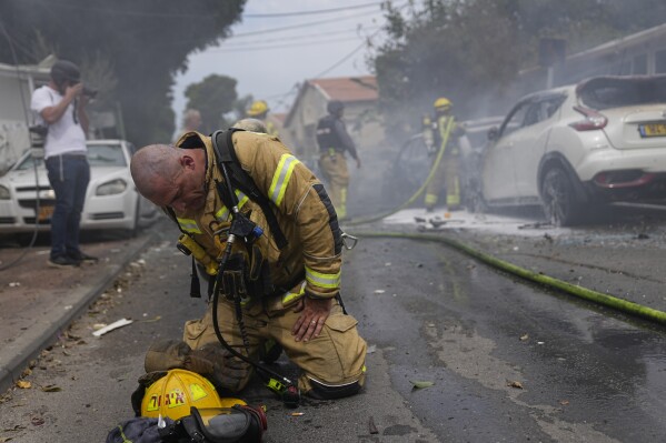 An Israeli firefighter kneels to compose himself after he and his colleagues extinguished cars set on fire by a rocket fired from the Gaza Strip in Ashkelon, Israel, Monday, Oct. 9, 2023. (AP Photo/Ohad Zwigenberg)