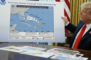 FILE - In this Sept. 4, 2019, file photo, President Donald Trump holds a chart as he talks with reporters after receiving a briefing on Hurricane Dorian in the Oval Office of the White House in Washington. Political pressure from the White House and a series of “crazy in the middle of the night” texts, emails and phone calls caused top federal weather officials to wrongly admonish a weather office for a tweet that contradicted President Trump about Hurricane Dorian in 2019, an inspector general report issued Thursday, July 9, 2020, found.  (AP Photo/Evan Vucci. File)