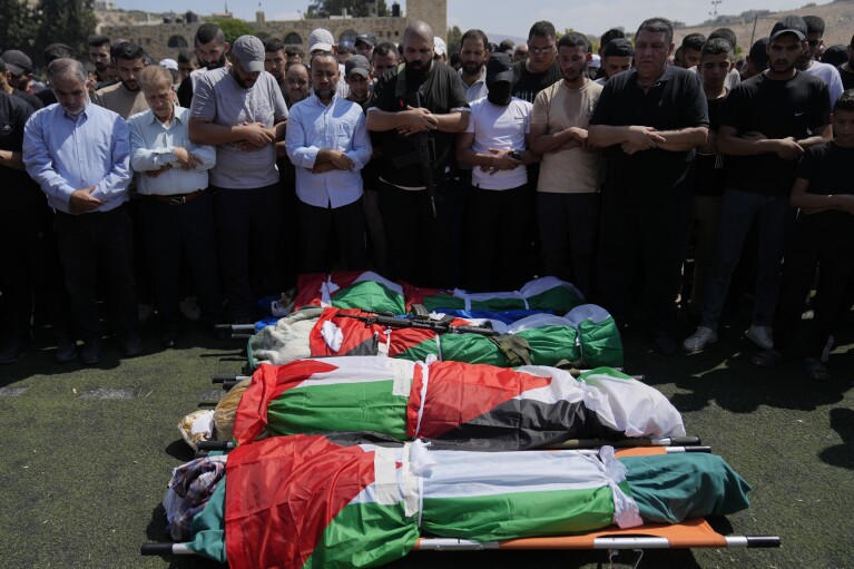 Mourners pray as they attend the funeral of four Palestinians, wrapped in Palestinian flags, who died during an Israeli military operation in the West Bank refugee camp of Al-Faraa, near Tubas, Thursday, Aug. 29, 2024. (AP Photo/Nasser Nasser)