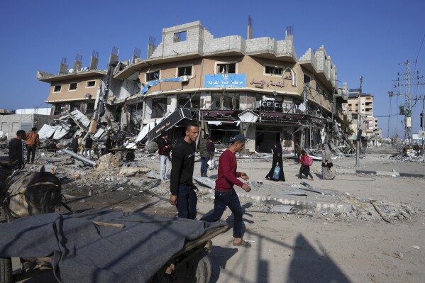 Palestinians walk through destruction by the Israeli bombardment in the Nusseirat refugee camp in Gaza Strip, Tuesday, Jan. 16, 2024. (AP Photo/Adel Hana)