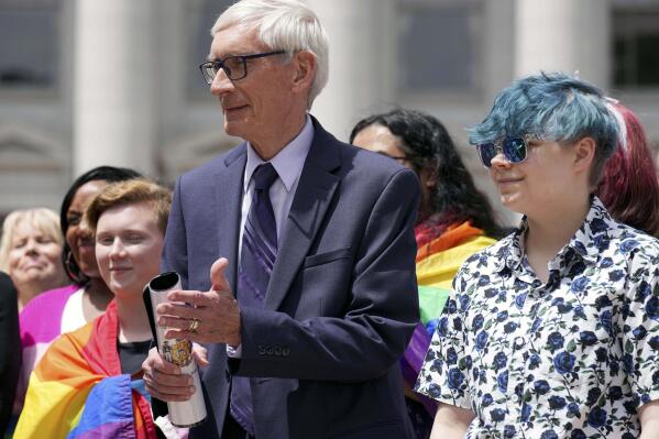 FILE - Wisconsin Gov. Tony Evers, left, stands next to 16-year-old Aspen Morris at the Rainbow Pride flag raising Wednesday, June 1, 2022 at the Capitol in Madison, Wis. Democratic political candidates who otherwise support the civil rights, safety and visibility of LGBTQ adults and children are finding it difficult to respond to a Republican vote-getting offensive targeting such people. The Republicans' use of LGBTQ people as a “wedge issue” seeks to appeal to the general public’s emotions and misunderstandings about transgender people in particular. (Mark Hoffman/Milwaukee Journal-Sentinel via AP File)