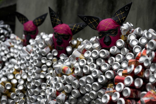 Fester klädda i kostymer gjorda av öl- och läskburkar deltar i karnevalsparaden för gatufesten 'Bloco da Latinha' i Madre de Deus, Brasilien, söndagen den 11 februari 2024. (AP Photo/Eraldo Peres)