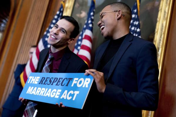 Equality Caucus Executive Director Jordan Dashow, left, and Equality Caucus Press Secretary Malachi White, right, pose with a sign that reads "The Respect For Marriage Act" after House Speaker Nancy Pelosi of Calif., accompanied by members of Congress, signed H.R. 8404, the Respect For Marriage Act, on Capitol Hill in Washington, Thursday, Dec. 8, 2022. (AP Photo/Andrew Harnik)