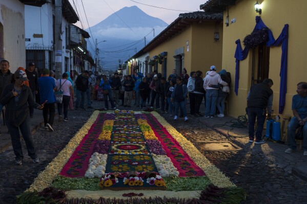 Faithful admire an elaborate carpet made of colored sawdust, fruits and vegetables made by Ivan Lemus and a dozen of his friends prior to the start of a Holy Week procession, in Antigua, Guatemala, on Good Friday, March 29, 2024. (AP Photo/Moises Castillo)