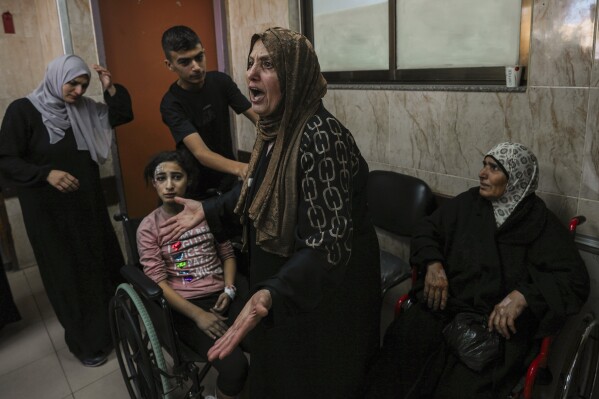 A Palestinian woman reacts next to people wounded in an Israeli airstrike, at al-Aqsa Hospital in Deir el-Balah, central Gaza Strip, Sunday, Oct. 15, 2023. (AP Photo/Adel Hana)