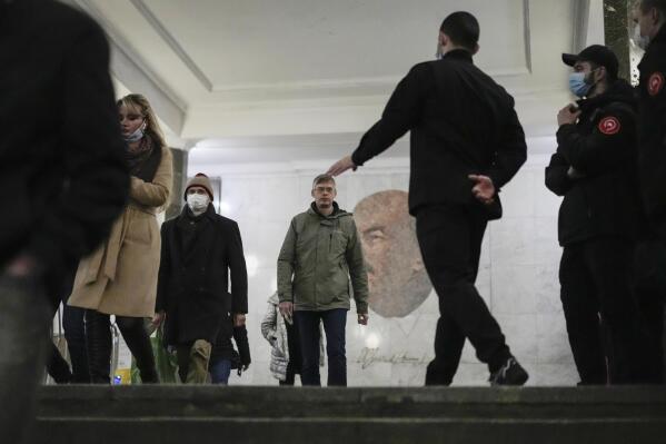 Moscow's metro security personnel, right, stops a passenger without a protective mask, with a portrait of Soviet founder Vladimir Lenin in the background, in Moscow, Russia, Monday, Oct. 25, 2021. Russia reported another daily record of confirmed coronavirus cases Monday as a surge in infections has prompted the Kremlin to tell most people to stay away from work starting later this week. (AP Photo/Pavel Golovkin)