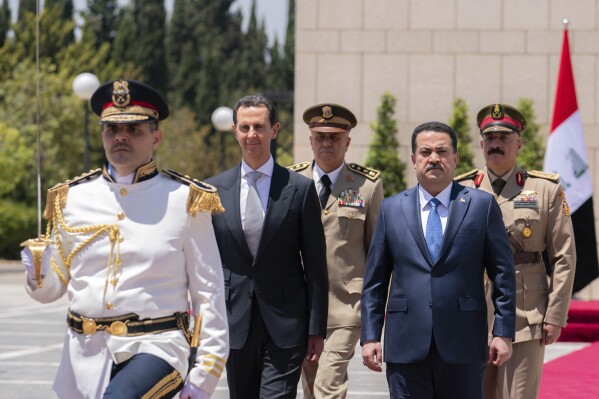 In this photo released by the Syrian official news agency SANA, Syrian President Bashar Assad, center left, and Iraq's Prime Minister Mohammed Shia al-Sudani review a military honour guard during a welcome ceremony in Damascus, Syria, Sunday, July 16, 2023. Iraq's prime minister held talks Sunday with Syrian President Bashar Assad in Damascus during the first such trip by an Iraqi premier to the war-torn country since the 12-year conflict began. (SANA via AP)