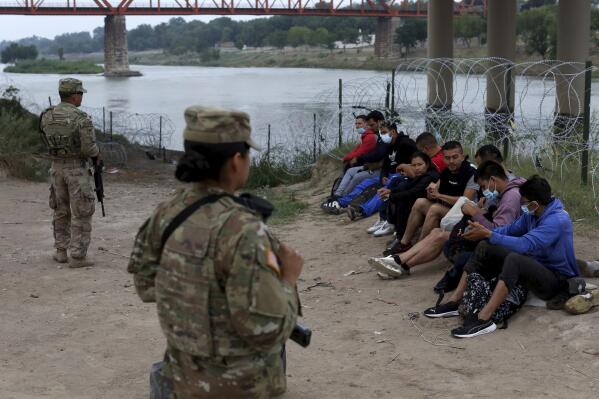 Migrants who had crossed the Rio Grande river into the U.S. are under custody of National Guard members as they await the arrival of U.S. Border Patrol agents in Eagle Pass, Texas, Friday, May 20, 2022. The Eagle Pass area has become increasingly a popular crossing corridor for migrants, especially those from outside Mexico and Central America, under Title 42 authority, which expels migrants without a chance to seek asylum on grounds of preventing the spread of COVID-19. A judge was expected to rule on a bid by Louisiana and 23 other states to keep Title 42 in effect before the Biden administration was to end it Monday. (AP Photo/Dario Lopez-Mills)