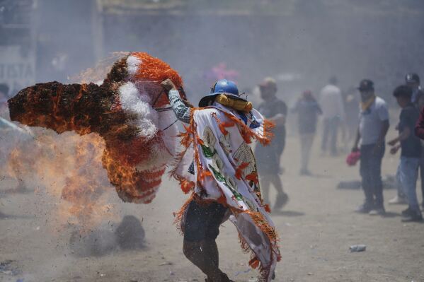 A reveler, known as a sayon, tries to put out a fire he started on his tissue paper hat as part of Easter celebrations in Tetela del Volcan, Mexico, Sunday, April 20, 2025. (AP Photo/Eduardo Verdugo)