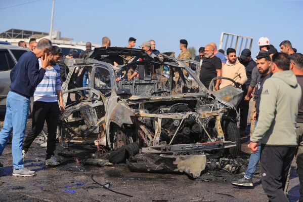 People gather near a charred car that was hit by an Israeli strike, in the southern coastal town of Ghazieh, Lebanon, Friday, April 18, 2025. (AP Photo/Mohammed Zaatari)