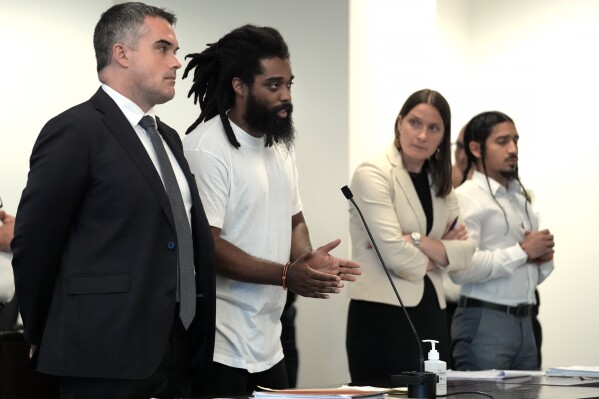 Jamhal Tavon Sanders Latimer, center left, addresses the judge while standing near defense attorney Daniel Thompson, left, defense attorney Josina Raisler-Cohn, center right, and Steven Anthony Perez, right, during a sentencing hearing for Latimer and Perez at Middlesex Superior Court, Tuesday, July 16, 2024, in Woburn, Mass. The two men were sentenced for their role in a 2021 armed standoff that shut down traffic on a busy highway in Massachusetts for more than eight hours. (AP Photo/Steven Senne)