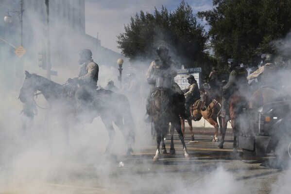 EDS NOTE: OBSCENITY - Tear gas surrounds law enforcement officers on horseback during a protest Saturday, June 14, 2025, in Los Angeles. (AP Photo/Ethan Swope)