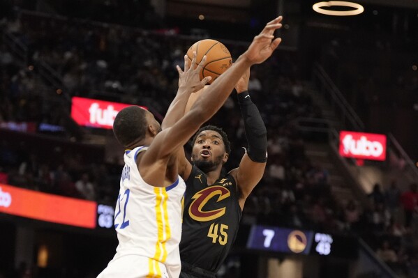 Cleveland Cavaliers guard Donovan Mitchell (45) shoots as Golden State Warriors forward Andrew Wiggins, left, defends in the second half of an NBA basketball game, Friday, Nov. 8, 2024, in Cleveland. (AP Photo/Sue Ogrocki)