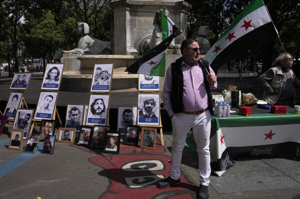 Activists hold Syrian flags next to portraits of alleged victims of the Syrian regime, during a demonstration Tuesday, May 21, 2024 at a courtroom in Paris. A Paris court will this week seek to determine whether Syrian intelligence officials — the most senior to go on trial in a European court over crimes allegedly committed during the country's civil war — were responsible for the 2013 disappearance and deaths of Patrick and Mazen Dabbagh. The four-day hearings, starting Tuesday, are expected to air chilling allegations that President Bashar Assad's government has widely used torture and arbitrary detentions to hold on to power during the conflict, now in its 14th year. (AP Photo/Michel Euler)