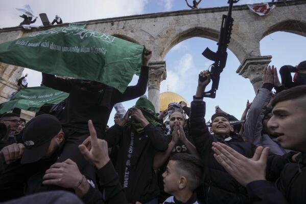 Palestinians brandish a toy gun and wave the flag of the Hamas militant group in protest against Israel, during Eid al-Fitr holiday celebrations by the Dome of the Rock shrine in the Al Aqsa Mosque compound in Jerusalem's Old City, Friday, April 21, 2023. The holiday marks the end of the holy month of Ramadan, when devout Muslims fast from sunrise to sunset. (AP Photo/Mahmoud Illean)