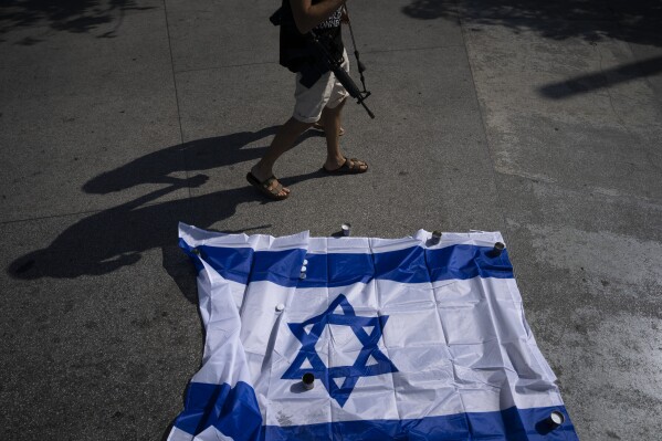 An off-duty Israeli soldier carrying a rifle walks by candles and the national flag honoring those who were killed or taken captive in a brutal cross-border attack by Hamas militants on Oct 7, in Tel Aviv, Israel, Wednesday, Oct. 25, 2023. More than 1,400 Israelis were killed, and over 200 people are being held hostage in Gaza. (AP Photo/Oded Balilty)