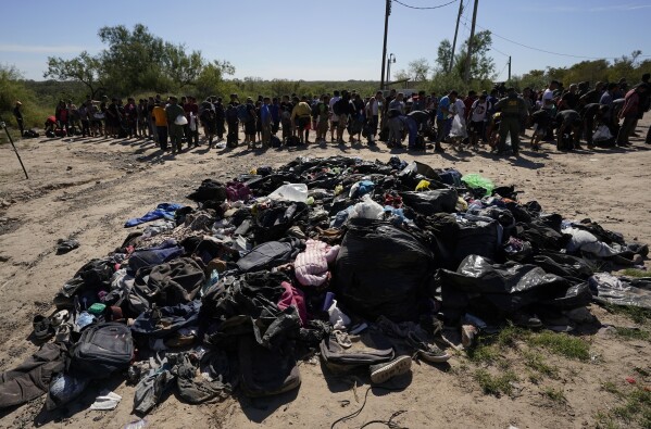 Migrants stand near a pile of discarded items as they wait to be processed by U.S. Customs and Border Patrol after crossing the Rio Grande and entering the United States from Mexico, on Thursday, October 19, 2023, in Eagle Pass, Texas.  (AP Photo/Eric Gay)