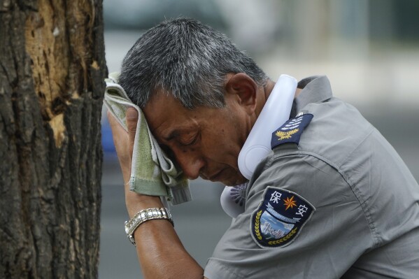 FILE - A security guard wearing an electric fan on his neck wipes his sweat on a hot day in Beijing, July 3, 2023. Climate change is making heat waves crawl slower across the globe and last longer with higher temperatures over larger areas, a new study finds. (AP Photo/Andy Wong, File)