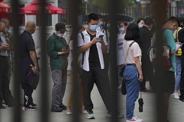 FILE - In this June 9, 2021, file photo, a man wearing a face mask to help curb the spread of the coronavirus browses his smartphone lining up with masked residents to receive their vaccine at a vaccination point at the Central Business District in Beijing. Chinese President Xi Jinping pledged 2 billion doses of Chinese vaccines would be supplied to the world through this year and $100 million would be donated to a U.N.-backed distribution program, state media reported. (AP Photo/Andy Wong, File)